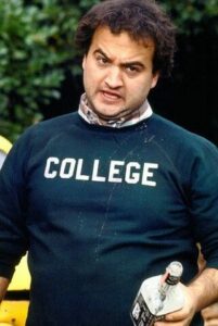 John Belushi in Animal House, wearing iconic College Sweatshirt while holding a bottle of Jack Daniels Whiskey